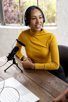 Woman recording podcast at home, wearing headphones and using microphone, smiling