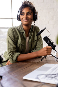 Young woman recording podcast at home, smiling with headphones and microphone