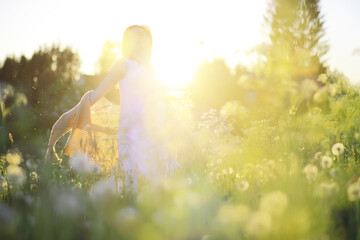 Pretty girl with a hat in her hand walks in a field with field flowers and smiles sincerely