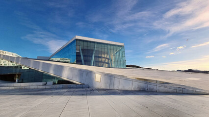 Oslo Opera House under a clear blue sky, featuring sleek glass facades and minimalist Scandinavian...