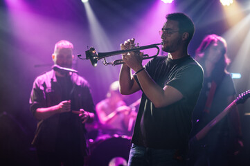 Trumpet player performing live on stage with band in purple light