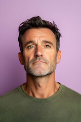 Fototapeta premium A mature man poses confidently against a soft purple backdrop, showcasing his distinctive features and relaxed demeanor while dressed casually in a green shirt