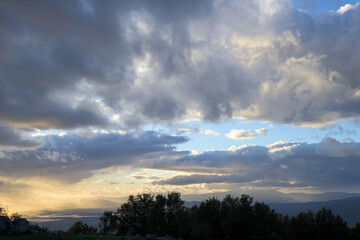 Cloud formation at sunset with blue sky and trees in foreground horizontally