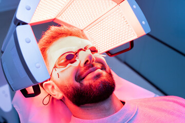 A young bearded Caucasian man in his 20s or 30s happily undergoes low-frequency hair laser therapy...