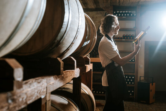 Winemaker Inspecting Bottle of White Wine in Cellar