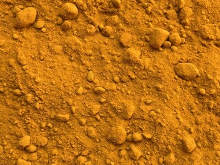 A close-up view of textured yellow powder, resembling a natural spice, with various small stones visible throughout the surface.