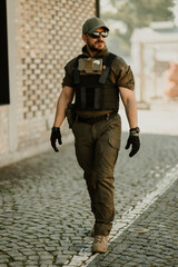 Soldier walking on cobblestone street wearing tactical gear and sunglasses