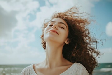 A relaxed woman enjoys the breeze at the seaside, with windswept hair and a refreshing sense of freedom.