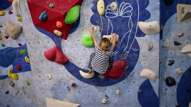 6-year-old boy practicing bouldering on a colorful indoor climbing wall. Focused and determined, he navigates different holds, showcasing strength and balance.