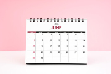 June 2025 desk calendar on white table with pink background.