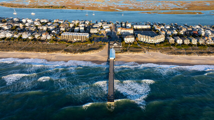 Aerial view of a pier stretching into the ocean at Wrightsville Beach, NC, surrounded by beachfront residential buildings and an inlet in the background.
