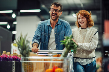 Happy couple pushing shopping cart in supermarket