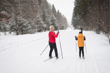Happy family winter fun - child and grandmother skiing at snowy forest