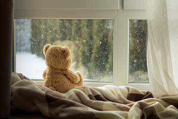 A teddy bear on a soft blanket by the window