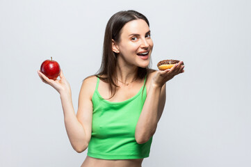 Beautiful young woman having to choose in between a donut and a red apple. On white background