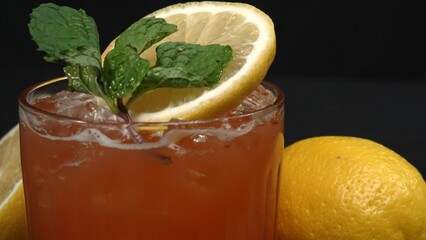 Macrography,of a Tequila Sunrise cocktail adorned with a slice of lemon and fresh mint leave, set against a dramatic black background. Close-up shot captures the vivid colors of cocktail. Comestible.