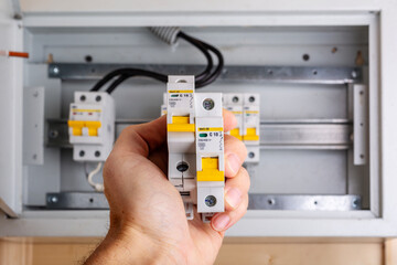 Hand holding two circuit breakers with yellow switches in front of a distribution box