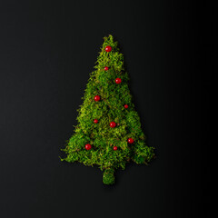 A creative Christmas tree made of moss with red ornaments on a black background. Minimalistic concept of Christmas and New Year.