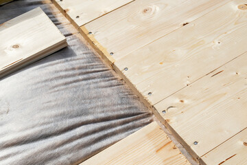 Close-up of wooden planks secured with screws over vapor barrier insulation for wooden house construction