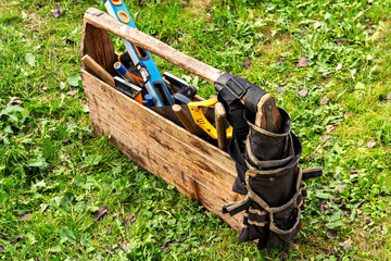 Fototapeta premium An old wooden toolbox with worn hand tools on grass, including a level, hammer, and tool belt