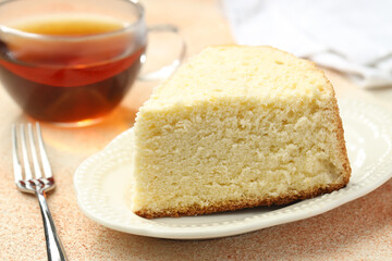 Piece of delicious sponge cake served on beige textured table, closeup