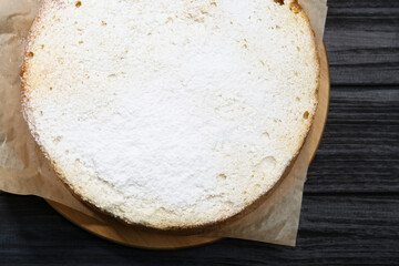 Delicious sponge cake with powdered sugar on black wooden table, top view
