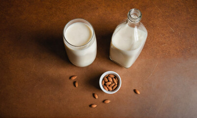 A glass of almond milk, a bottle of almond milk, and a small bowl of almonds sit on a brown surface