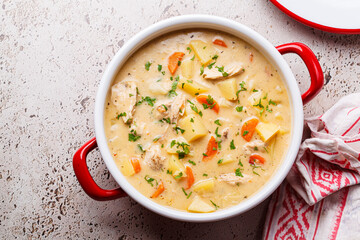 Chicken stew in creamy sauce with potatoes and carrots in red saucepan. Comfort food concept.