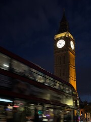 A mesmerizing night view of Big Ben, illuminated against the dark sky. A red double-decker bus...