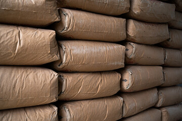 A stack of bags of cement. The bags are brown and stacked on top of each other. The bags are piled...