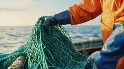 A fisherman in an orange waterproof suit gathers green fishing nets at sunset by the sea, showcasing the essence of the fishing industry.