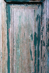 Detail of old front damaged door, green painting is peeling on the wood. Close-up