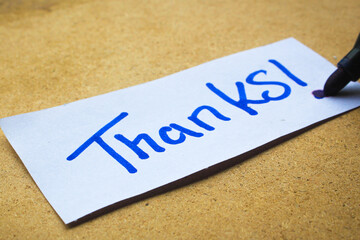 A handwritten note saying "Thanks!" in blue ink on a piece of white paper, placed on a light brown surface. Perfect for themes of gratitude, appreciation, and positive communication.