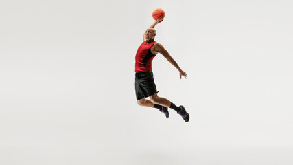 Middle-aged, skilled man in sleeveless jersey and shorts jumps to shoot basketball against grey studio background. Concept of sport event, competition, active and healthy lifestyle, game.