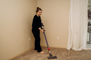 A girl in a black housecoat is vacuuming a coffee-colored carpet.