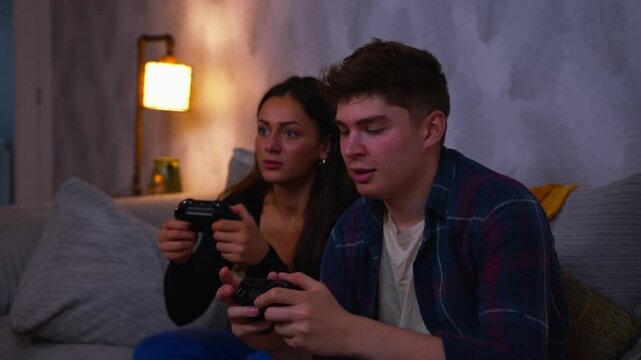Cute couple playing video games on the sofa together boyfriend wins the game and celebrates