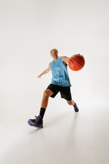 Fototapeta premium Middle aged basketball athlete dressed in sportswear dribbles basketball, ready to make shot against grey studio background. Concept of sport event, competition, active and healthy lifestyle, game.