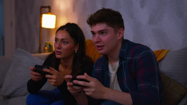 Cute couple playing video games on the sofa together girlfriend celebrates and boyfriend loses