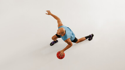 Middle aged man, basketball athlete in sports gear dribbles basketball, preparing for his next dunk against grey studio background. Concept of sport event, competition, healthy lifestyle, game. © Lustre Art Group 