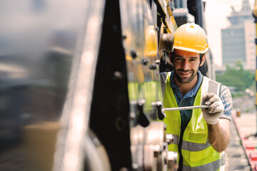 A man in a yellow hard hat is working on a piece of machinery. He is smiling and he is enjoying his work