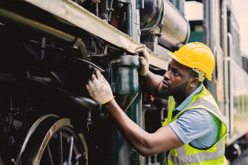 A man in a yellow helmet is working on a train engine. He is wearing a safety vest and gloves