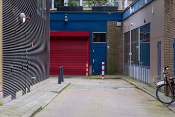A vibrant alleyway exhibits contrasting red and blue hues, with a prominently painted garage door, creating an inviting and lively urban landscape.