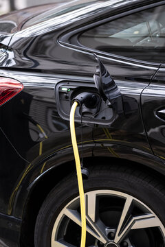 A sleek black electric car is parked and being charged with a yellow cable, showcasing the progress and sustainability in automotive technology, taken indoors.