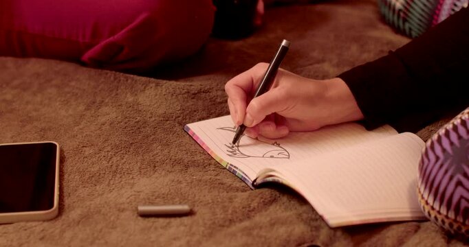Person is sketching fish creatively in notebook, sitting comfortably on soft surface. Reflect a journey of self-discovery, where conversations at home encourage reflection and personal growth.