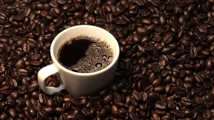 Top view of coffee or espresso with piles of coffee beans. Close up of fresh roasted coffee bean scatter around wooden table with cup of americano and aromatic stream and smoke from seed. Comestible.