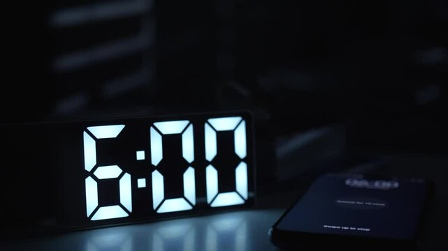 Digital alarm clock and smartphone waking up at 6 am, close-up. Mobile phone and alarm clock on nightstand