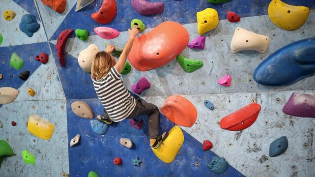 6-year-old boy practicing bouldering on a colorful indoor climbing wall. Focused and determined, he navigates different holds, showcasing strength and balance.