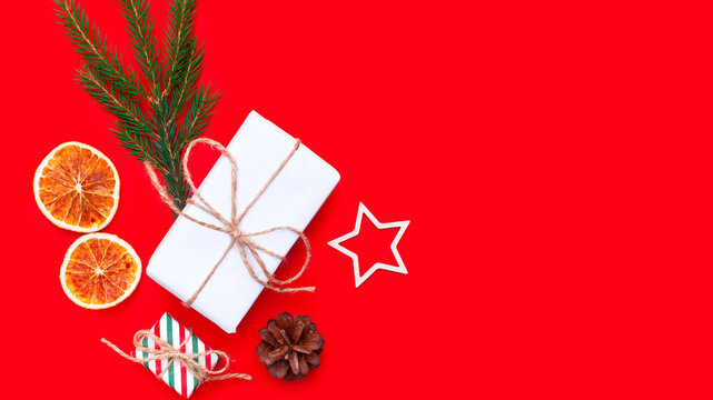 Collection of Christmas objects - goft box, eve fir, dried orange, pine cone, star cinnamon on red background. New Year and winter minimal holiday frame composition. Flat lay, top view, place for text