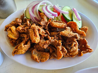 A plate of Fish crackling with a side of vegetables. The vegetables include onions, cucumbers, and tomatoes