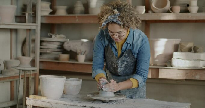Slow motion of African American potter working with clay on throwing wheel enjoying hobby in workshop. Creative people and small business concept.